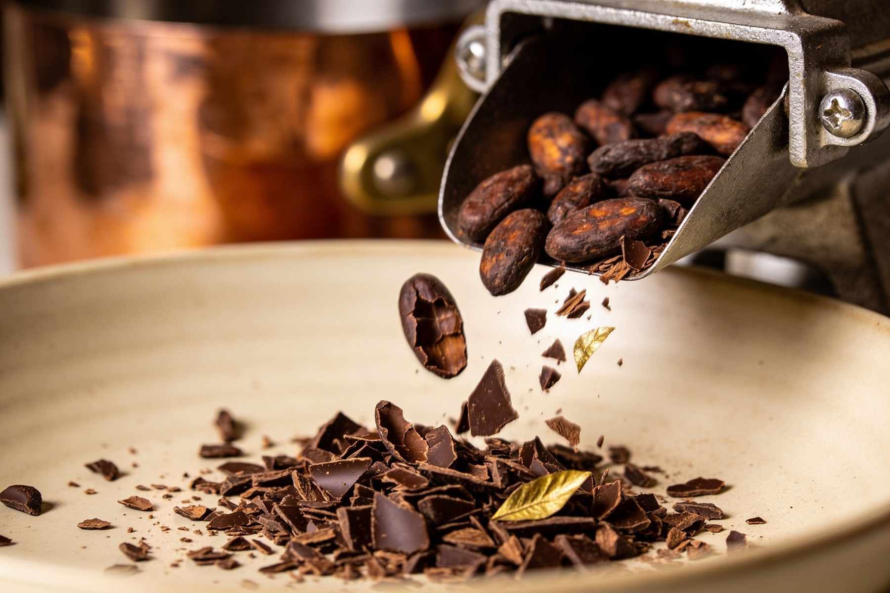 Roasted cacao beans being cracked and winnowed into nibs, a copper roaster in the background.