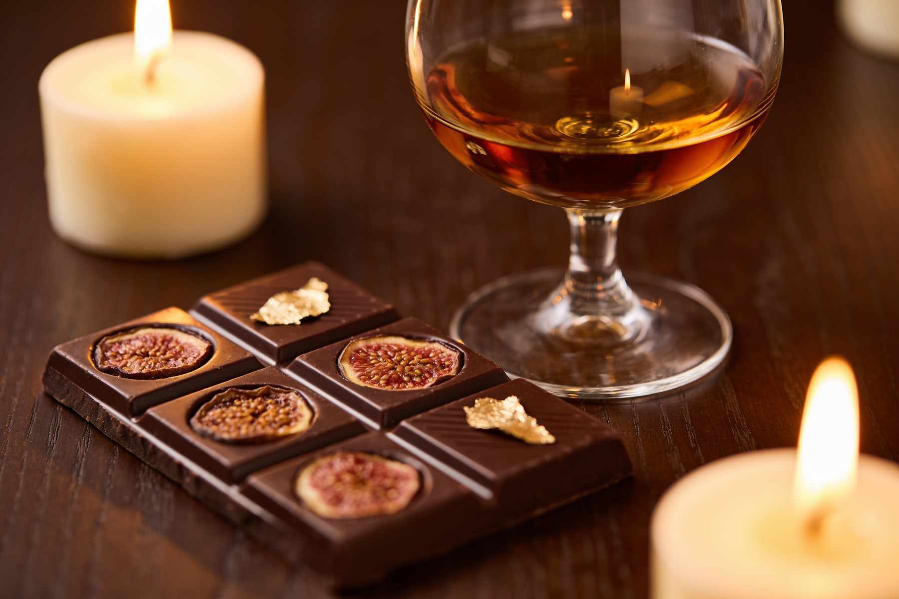 A glass of tawny port and squares of dark chocolate with dried figs on a dark table by candlelight.