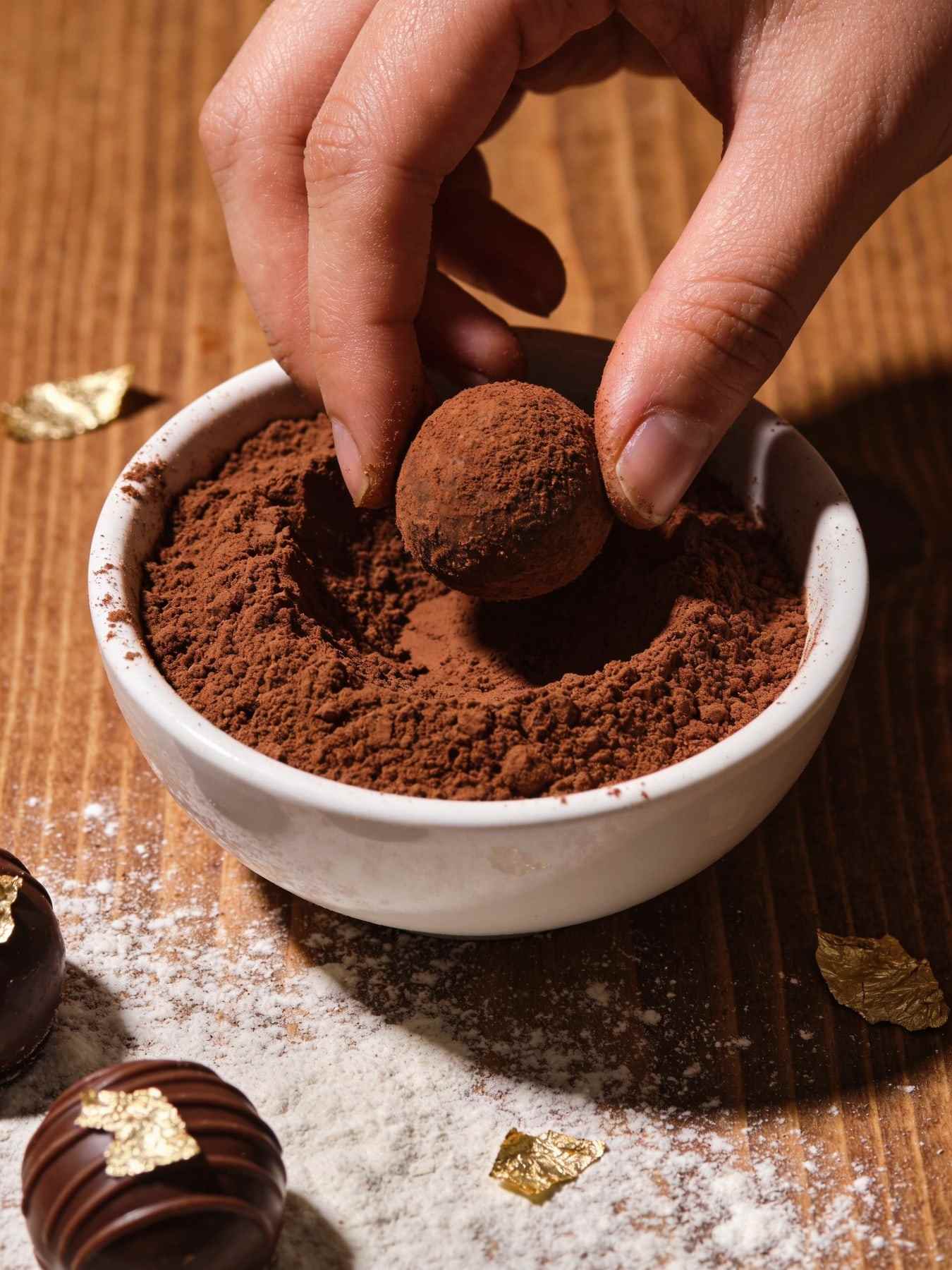 Hands rolling cocoa-dusted truffles in a bowl of cocoa powder.