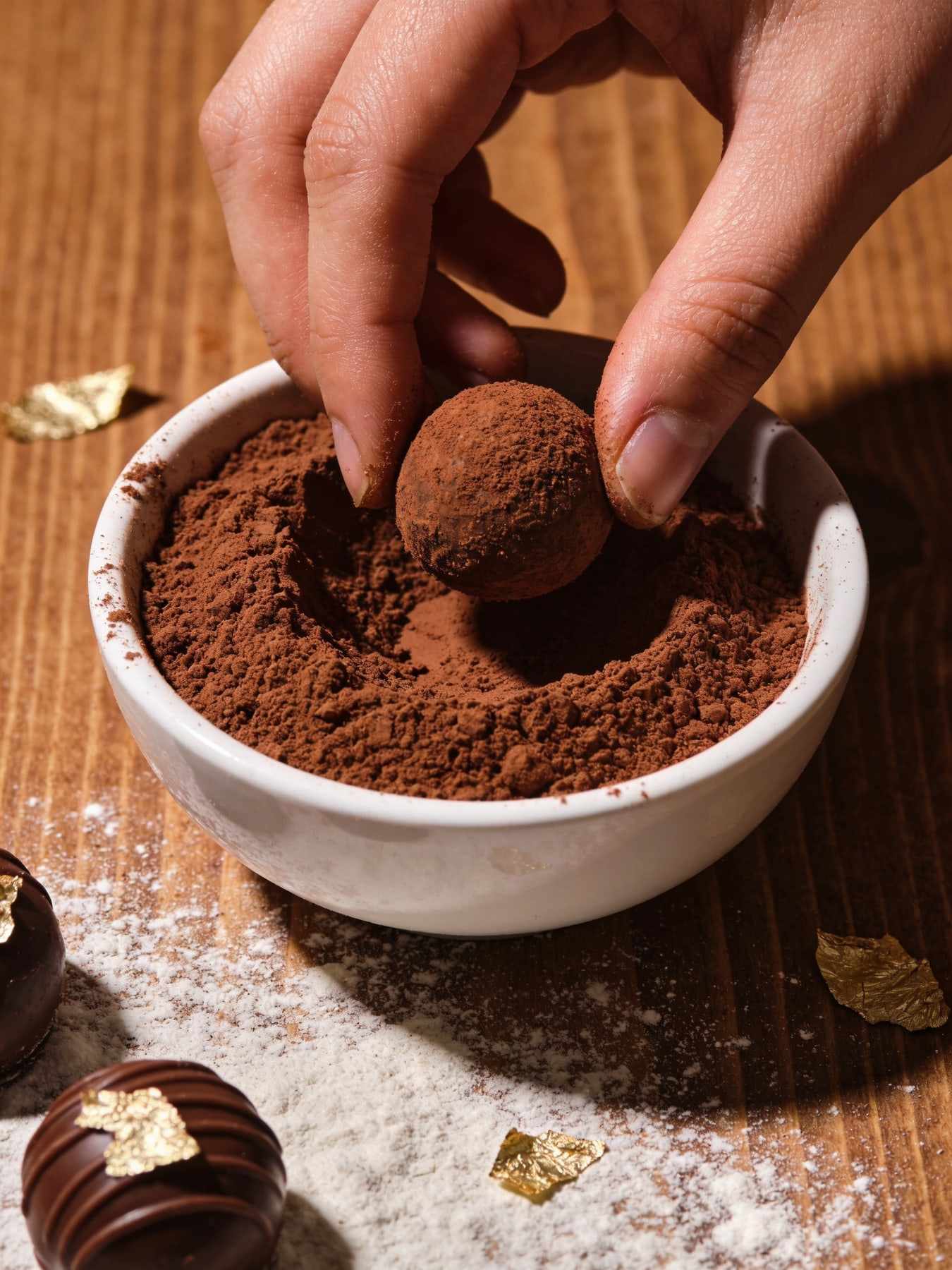 Hands rolling cocoa-dusted truffles in a bowl of cocoa powder.